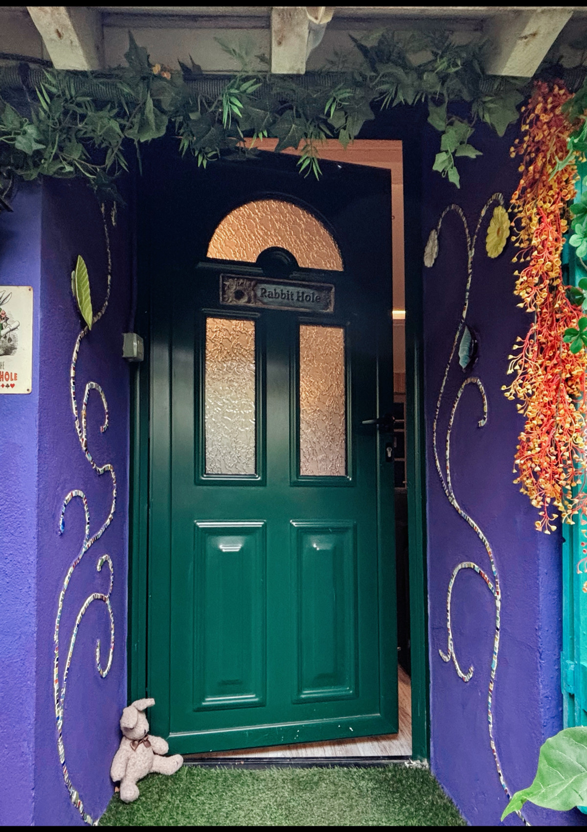 Entrée féerique Wonderland21 avec porte verte ornée de motifs dorés et mur violet